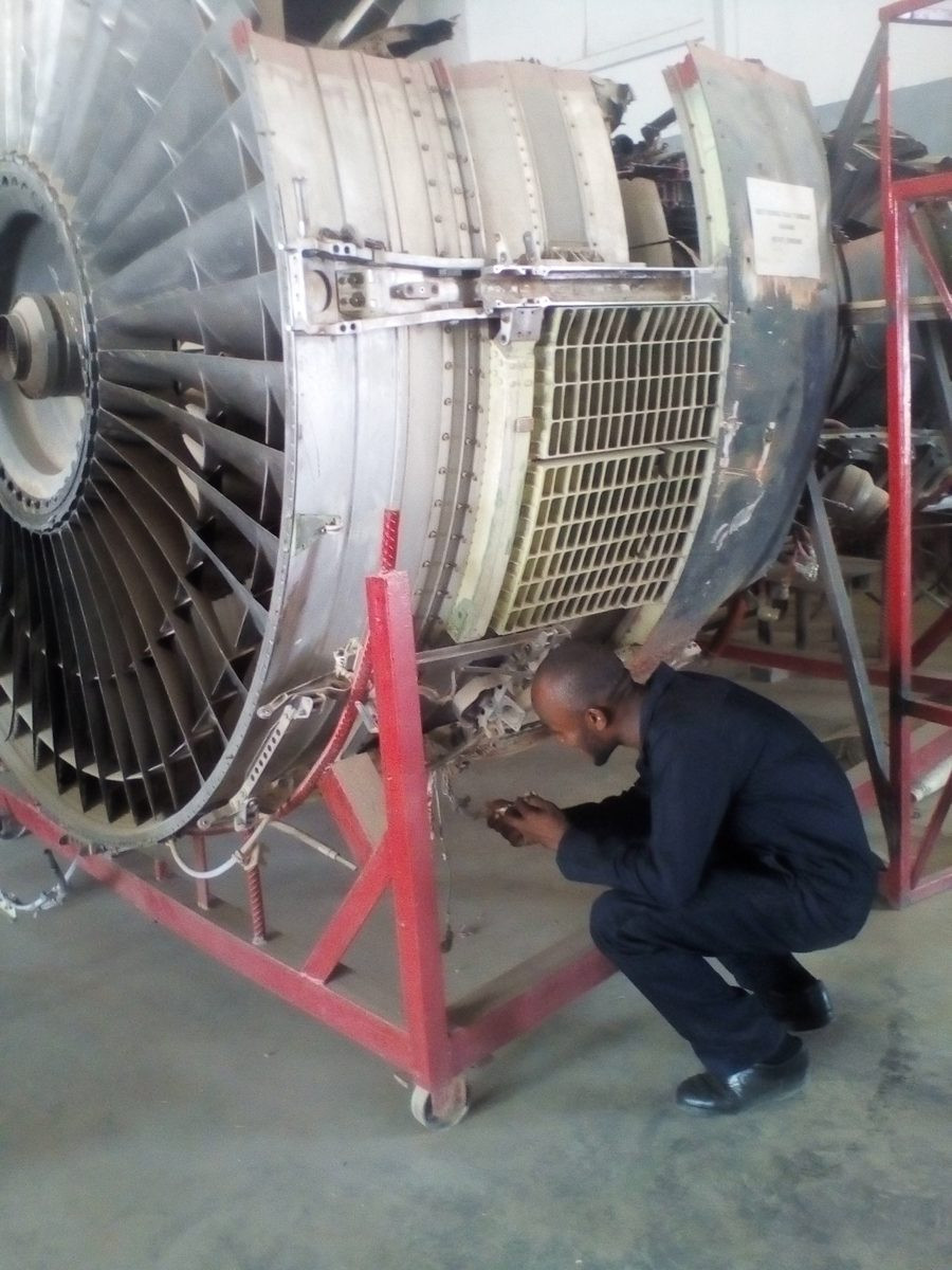 Ugochukwu crouching beside a large aircraft engine on a stand.