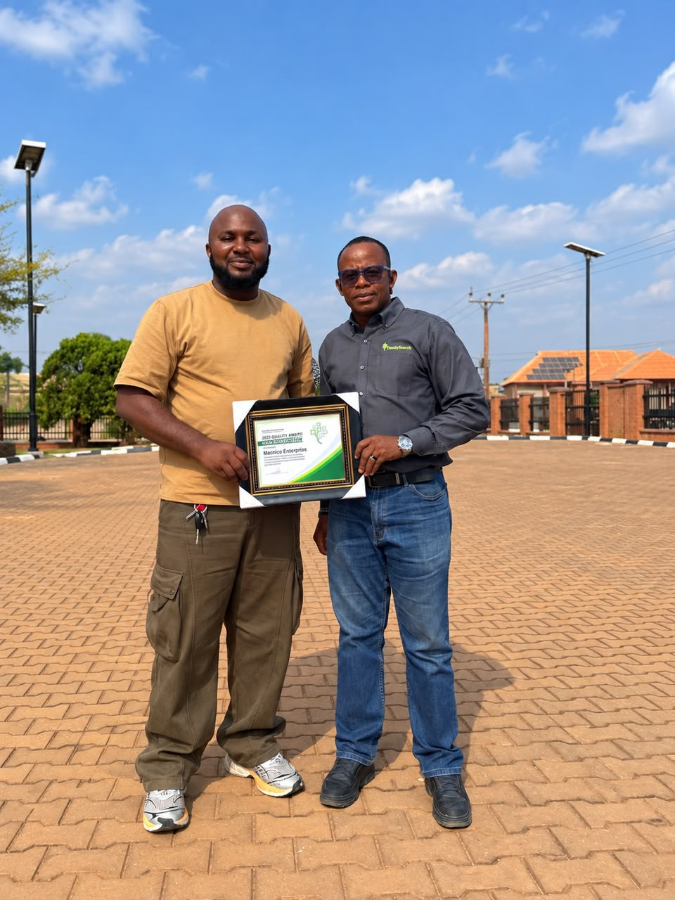 Ikegbunem Ugochukwu and the FamilySearch country manager holding the framed Quality Award certificate outdoors.