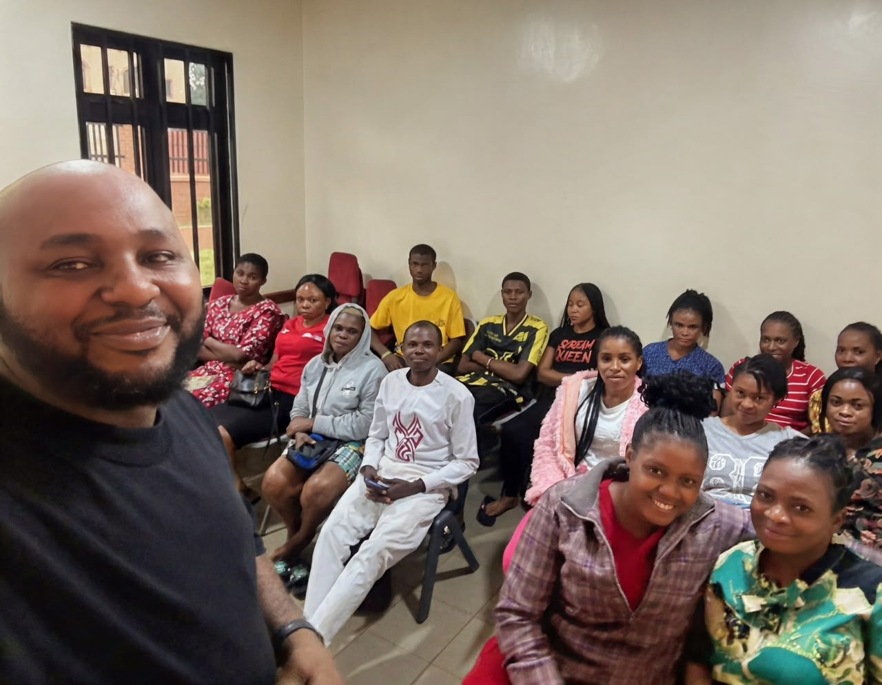 Ikegbunem Ugochukwu taking a selfie with a seated group of about fifteen team members in a meeting room.