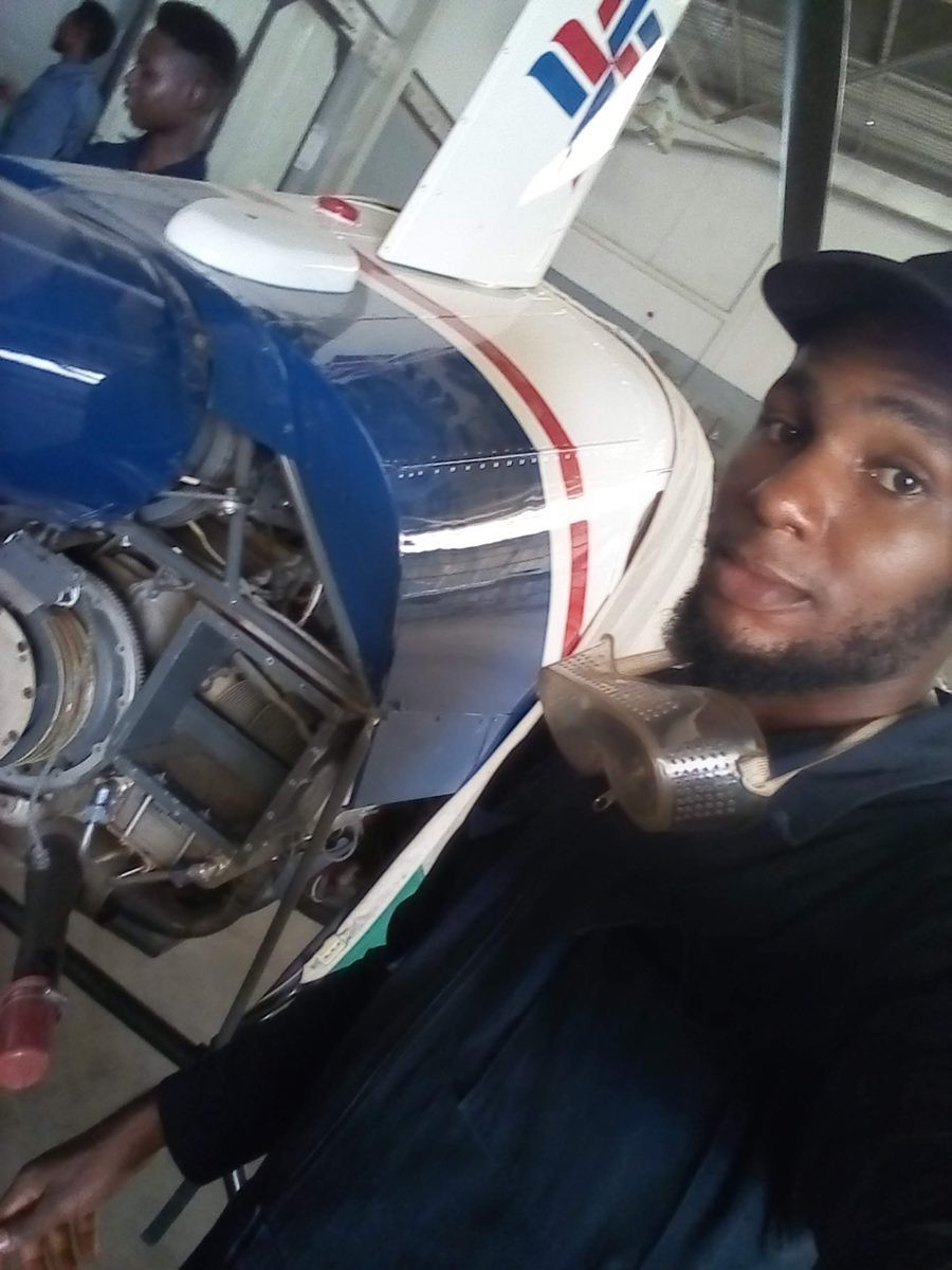 Ugochukwu taking a selfie beside an aircraft engine in a hangar.