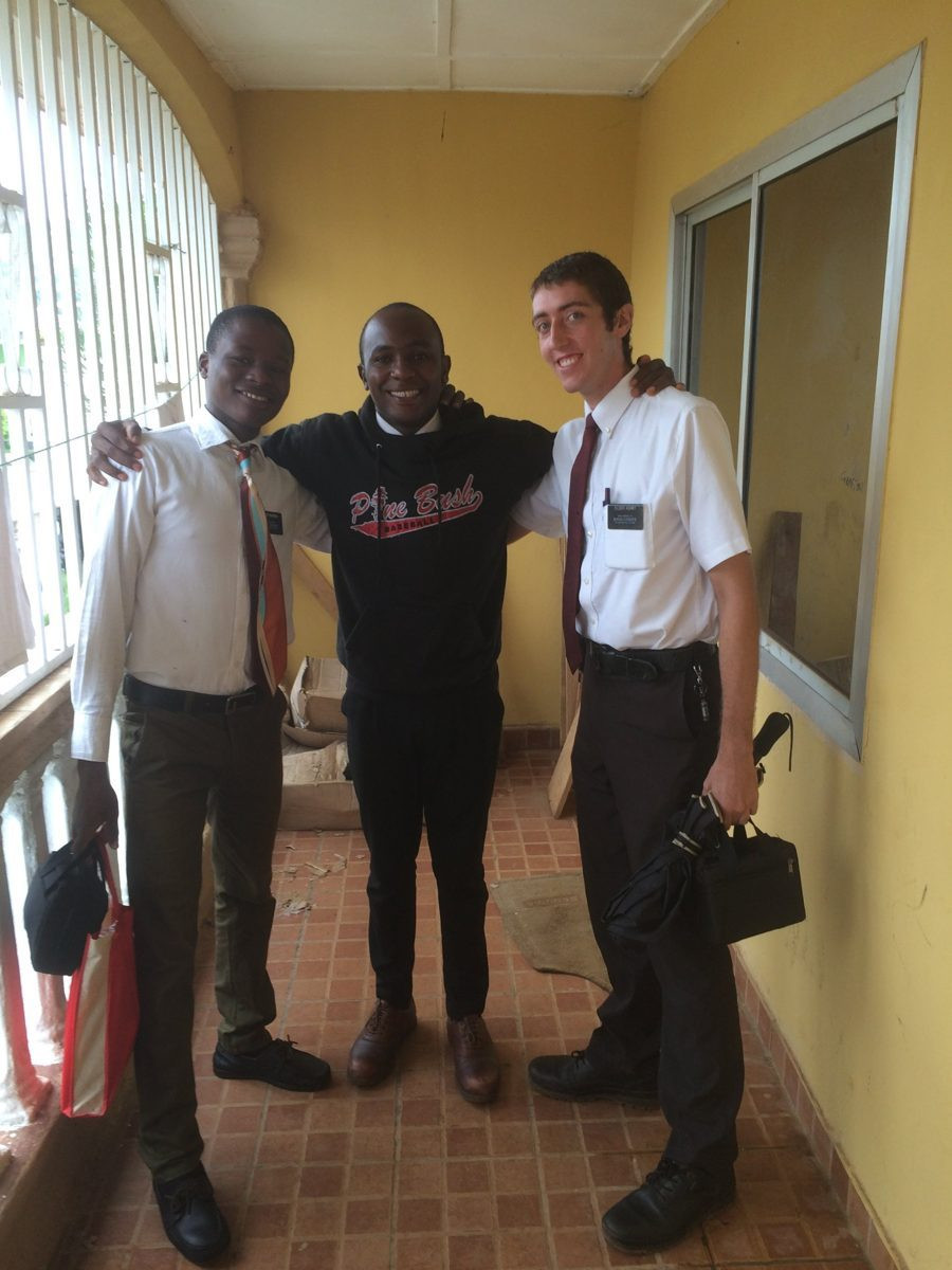 Three men standing together indoors; two wear white shirts and ties.